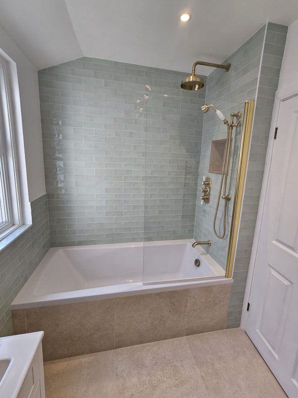 A bath-and-shower combination with a quality glass screen, light blue subway tile and brass brassware — still the safest choice for family-target London homes.