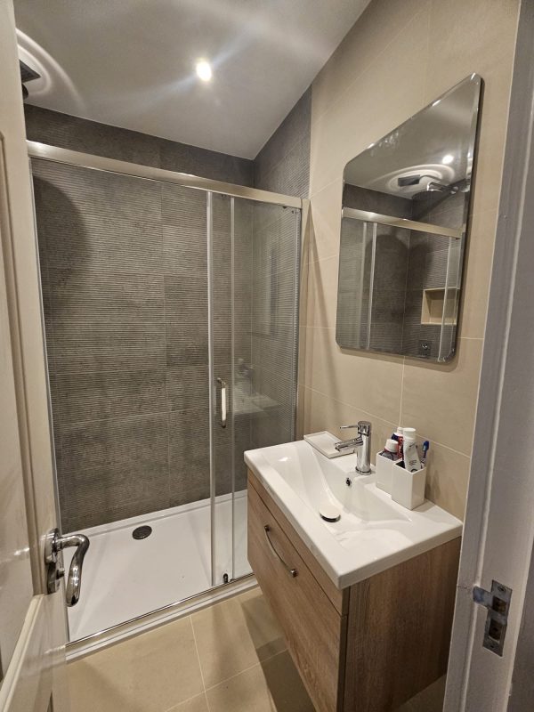 A walk-in shower in a compact London bathroom — the sliding glass enclosure contains the wet zone and reduces the waterproofing burden.