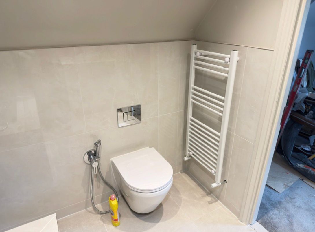 A real compact London bathroom — wall-hung WC and slim radiator make the most of a tight footprint under a sloped ceiling.