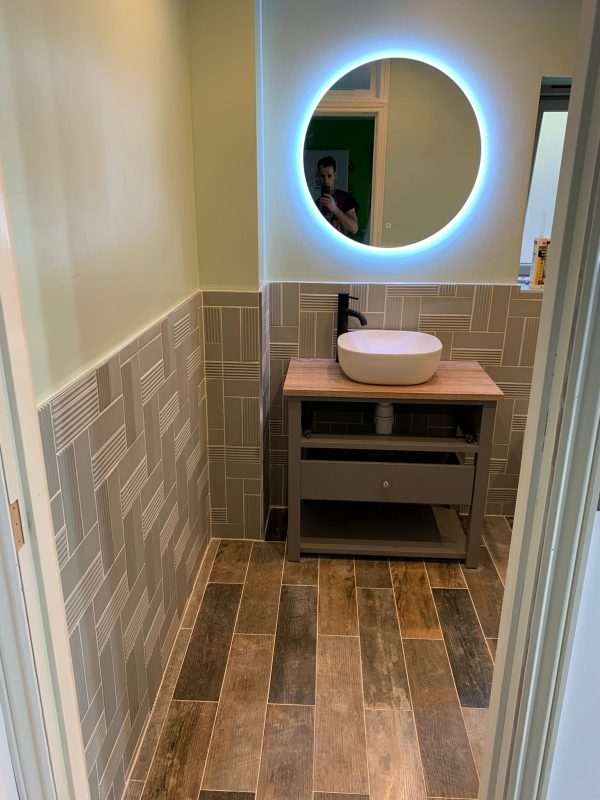 Backlit mirror as the primary light source — typically £200–£600 of spend that transforms a windowless bathroom more than tile choice does.