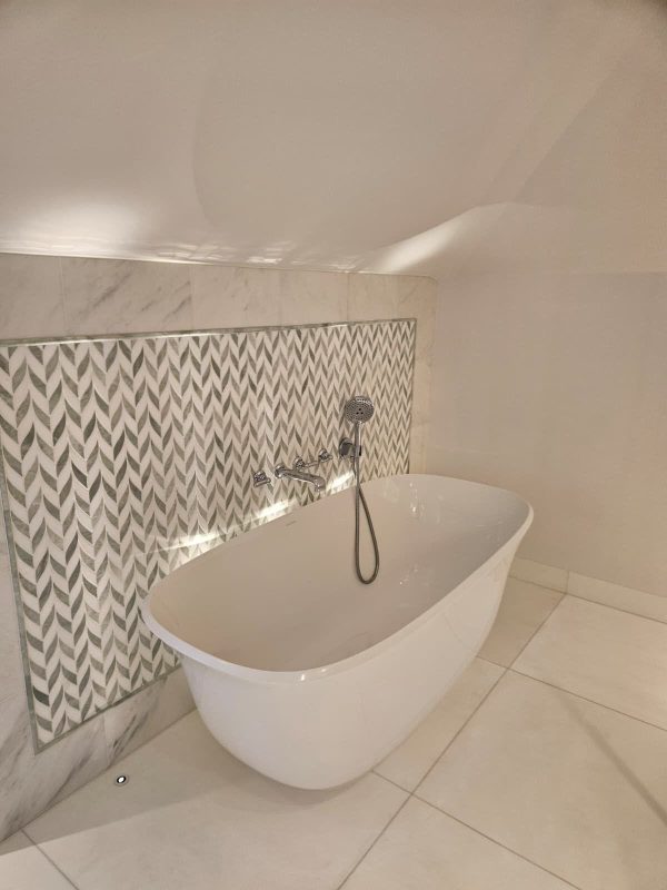 A freestanding bath set against a herringbone feature tile — a traditional bath remains the strongest format for family-target homes.